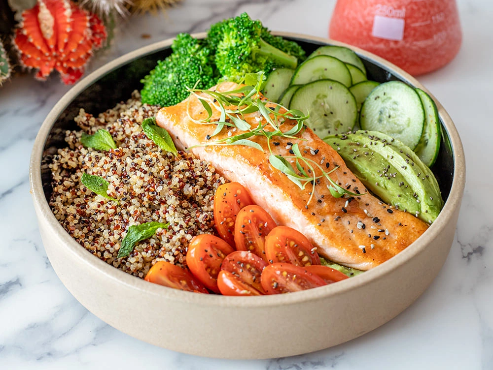 A dinner plate with baked salmon, fluffy quinoa, and steamed broccoli, garnished with a lemon wedge.