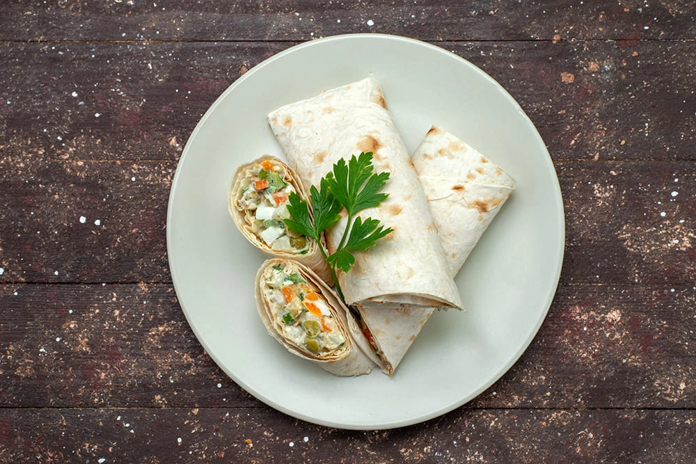 Plate of tortilla wraps filled with a creamy vegetable and cheese mixture, garnished with fresh parsley, set on a rustic dark wooden surface