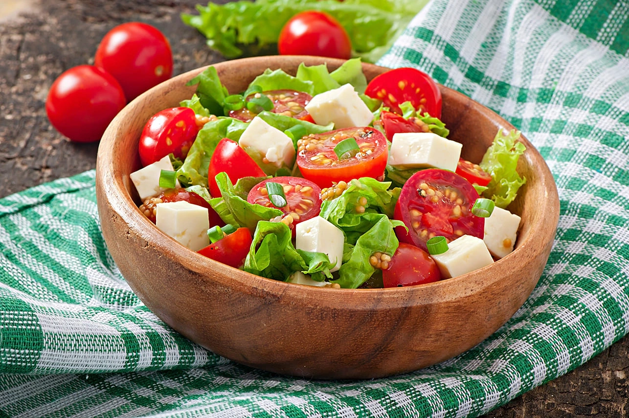 Fresh salad with cherry tomatoes, lettuce, and cottage cheese cubes in a wooden bowl