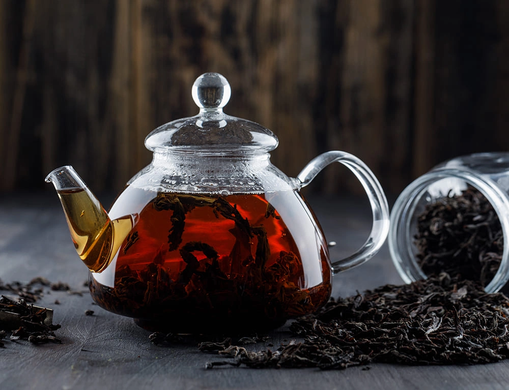 Clear teapot filled with dark Keemun tea beside loose leaves