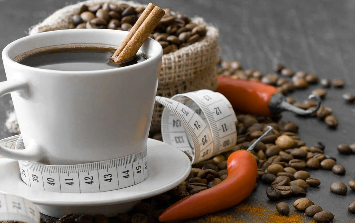 Cup of black coffee with a cinnamon stick, surrounded by coffee beans, red chili peppers, and a measuring tape symbolizing weight loss