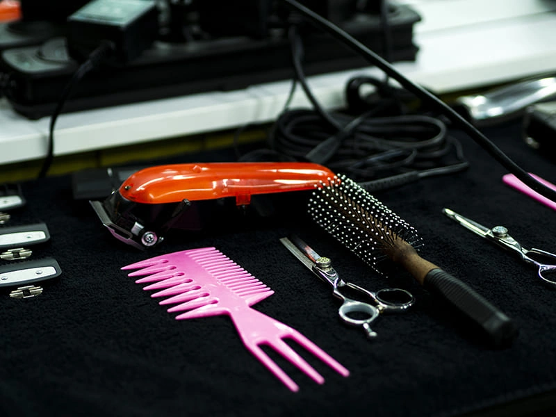 Barber tools including hair clippers, scissors, combs, and a round brush arranged on a black towel.