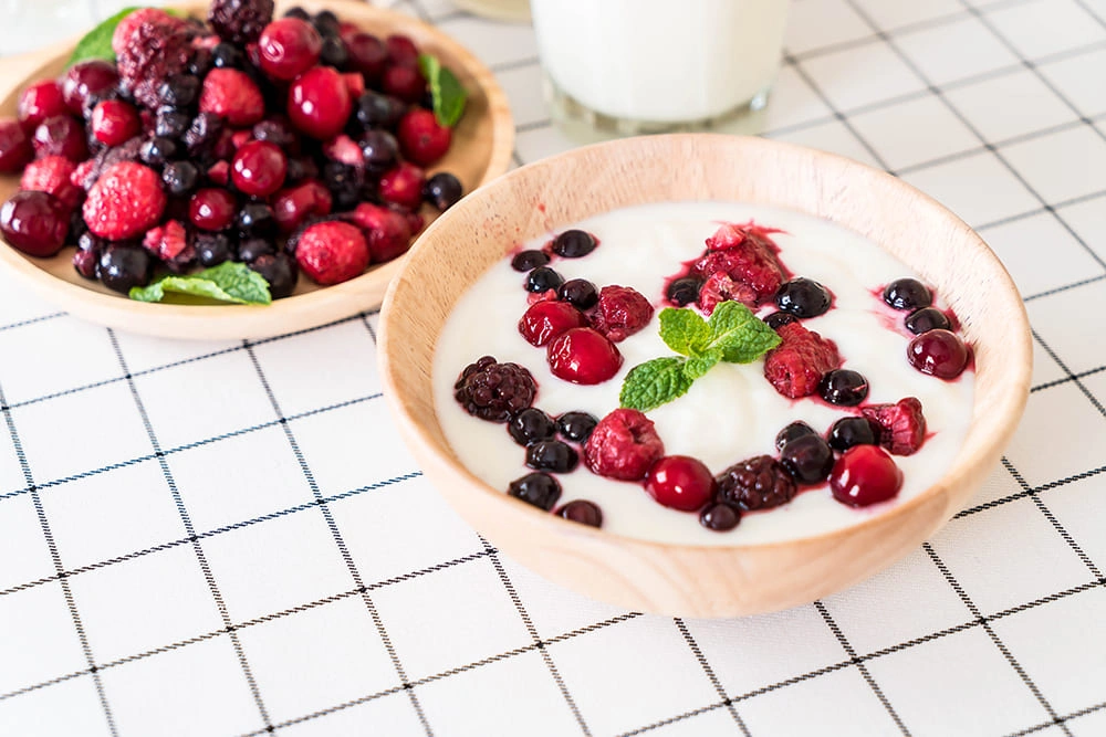 A white bowl of plain Greek yogurt topped with blueberries, strawberries, chia seeds, and a few almonds.