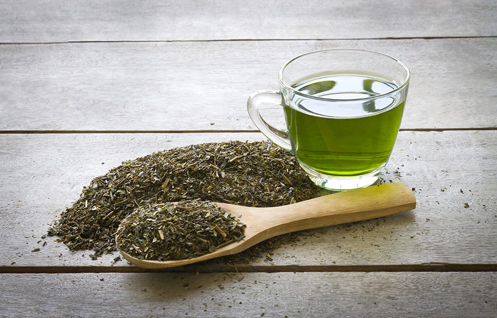 Gunpowder green tea leaves with brewed tea in a glass cup