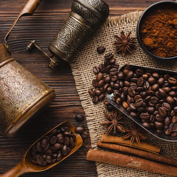 Traditional coffee setup with roasted coffee beans, ground coffee, spices, and antique brass utensils on a rustic wooden table