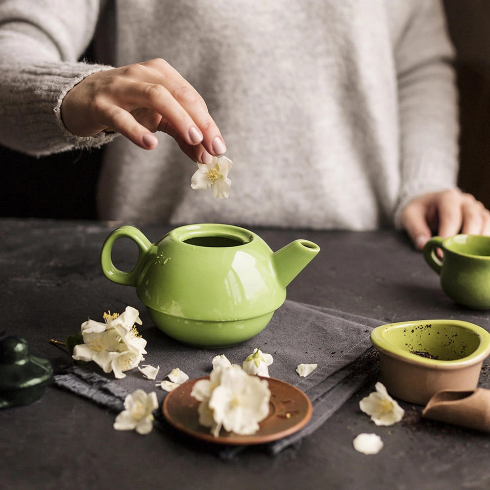 Hand placing jasmine flower in green teapot
