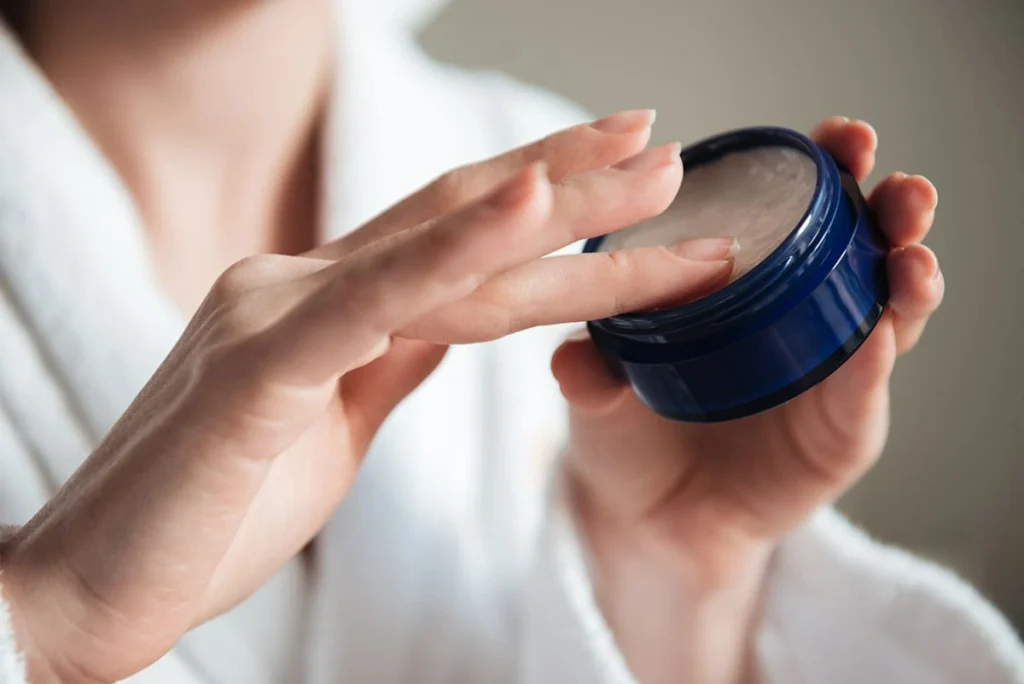 Woman using petroleum jelly from a blue container to soften and remove super glue from skin