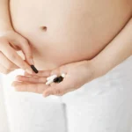Close-up of a pregnant woman holding various pills in her hand, considering supplement or medication options.