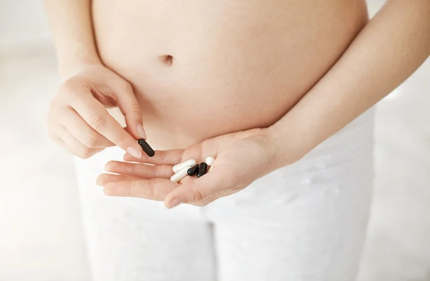 Close-up of a pregnant woman holding various pills in her hand, considering supplement or medication options.