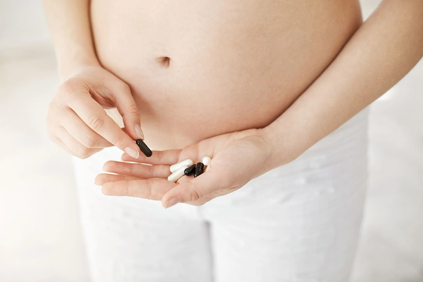 Close-up of a pregnant woman holding various pills in her hand, considering supplement or medication options.