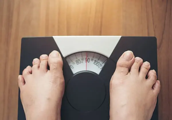 Person standing barefoot on an analog bathroom scale, checking weight as part of a weight loss routine.