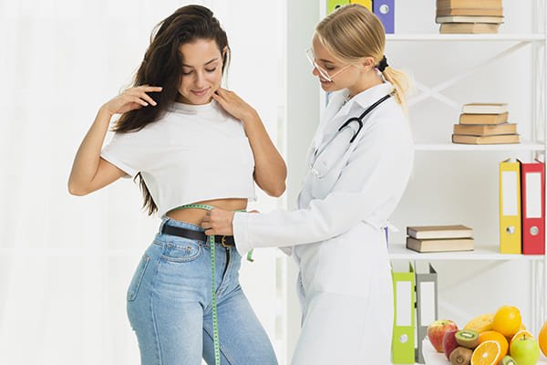 Female doctor measuring young woman’s waist as part of a weight loss check-up and fitness progress evaluation.