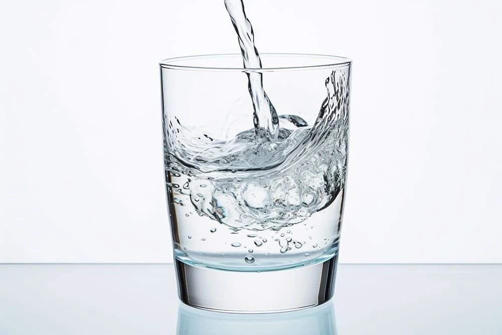 Clear sparkling water being poured into a transparent glass with visible bubbles.
