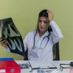 Female doctor looking concerned while analyzing chest X-ray scans, surrounded by medical supplies