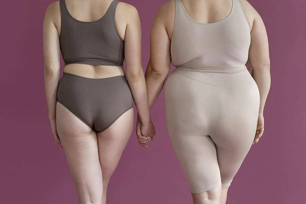 Rear view of two women with different body types holding hands, showcasing body positivity and diversity in shape.